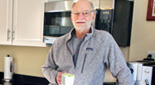 Michael Rosbash leans against a counter in his kitchen, holding a mug.